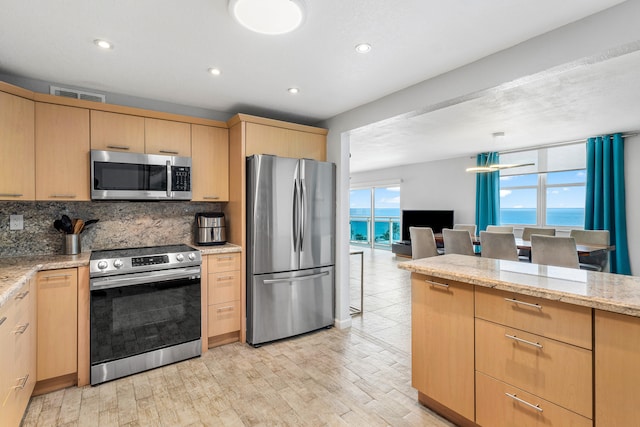 kitchen featuring appliances with stainless steel finishes, light brown cabinets, light hardwood / wood-style flooring, and light stone counters