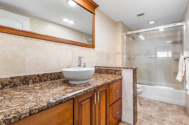 full bathroom featuring toilet, tile walls, bath / shower combo with glass door, vanity, and tile patterned flooring