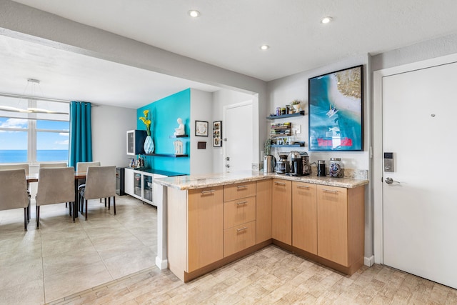 kitchen featuring a water view, light stone counters, light brown cabinetry, and kitchen peninsula