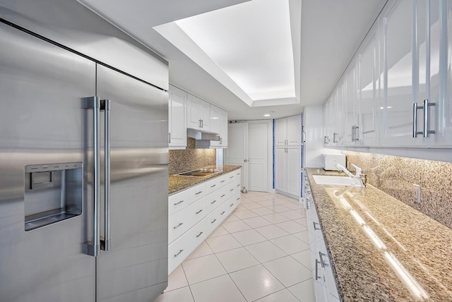 kitchen with high quality fridge, black electric cooktop, a tray ceiling, dark stone countertops, and white cabinetry