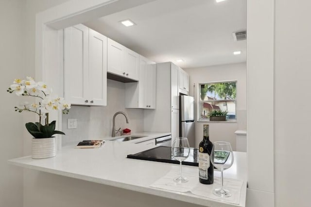 kitchen featuring kitchen peninsula, white cabinets, sink, and stainless steel refrigerator