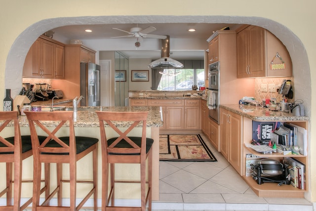 kitchen featuring light stone countertops, light brown cabinetry, kitchen peninsula, stainless steel appliances, and a breakfast bar area