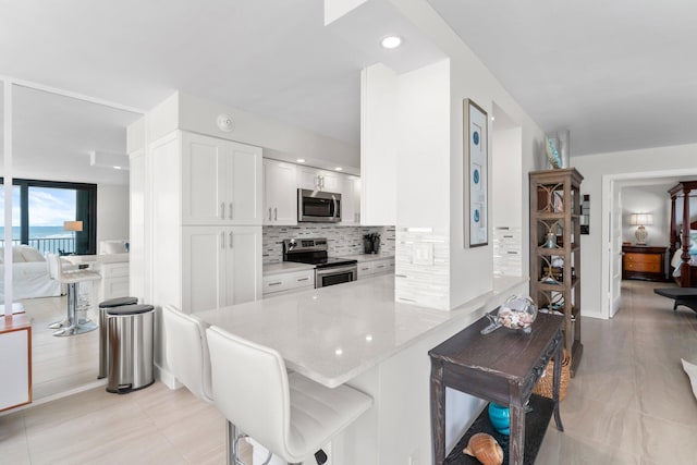 kitchen featuring a kitchen breakfast bar, kitchen peninsula, decorative backsplash, appliances with stainless steel finishes, and white cabinetry