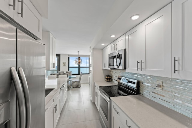 kitchen with appliances with stainless steel finishes, tasteful backsplash, light tile patterned floors, white cabinetry, and hanging light fixtures