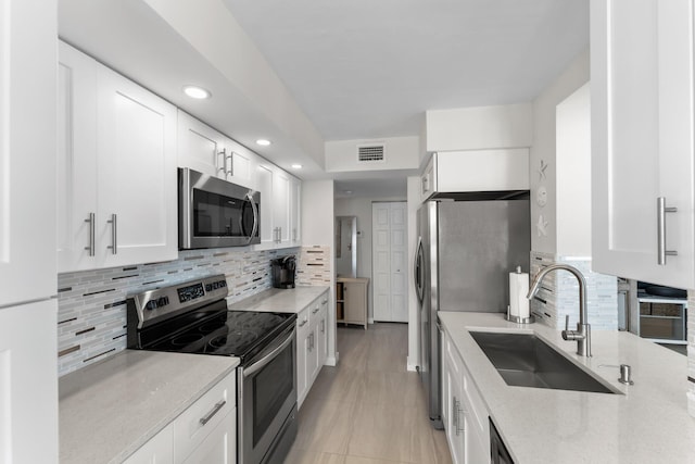 kitchen with backsplash, white cabinets, sink, appliances with stainless steel finishes, and light stone counters