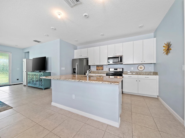 kitchen featuring stainless steel appliances, a textured ceiling, a center island with sink, and white cabinets