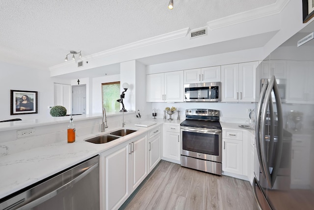 kitchen with white cabinets, appliances with stainless steel finishes, light hardwood / wood-style floors, crown molding, and sink