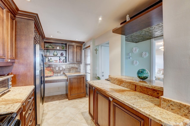 kitchen featuring light stone countertops, decorative backsplash, stove, stainless steel refrigerator, and light tile patterned floors