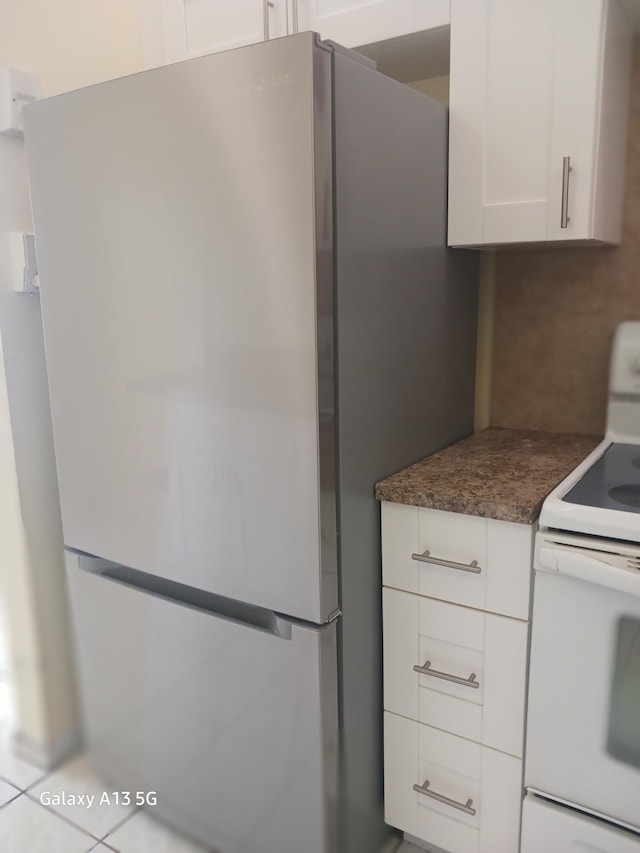 kitchen with backsplash, light tile patterned floors, white cabinets, stainless steel refrigerator, and electric stove