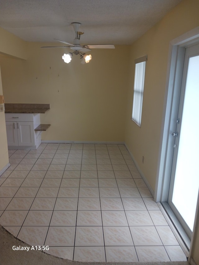 unfurnished dining area featuring a textured ceiling, light tile patterned floors, and ceiling fan