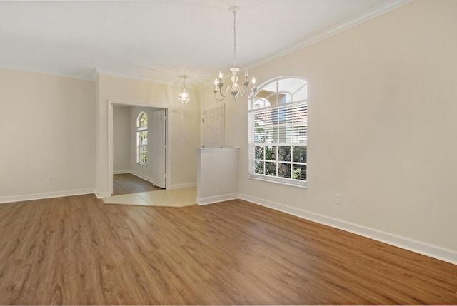 unfurnished room with wood-type flooring, an inviting chandelier, ornamental molding, and a healthy amount of sunlight