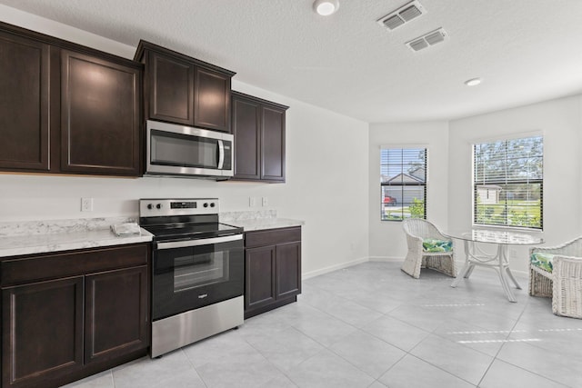 kitchen with a textured ceiling, dark brown cabinetry, stainless steel appliances, and light tile patterned floors