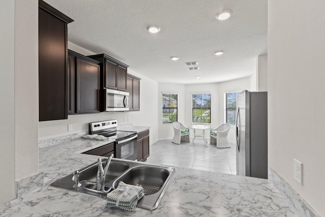 kitchen with kitchen peninsula, appliances with stainless steel finishes, dark brown cabinets, and sink