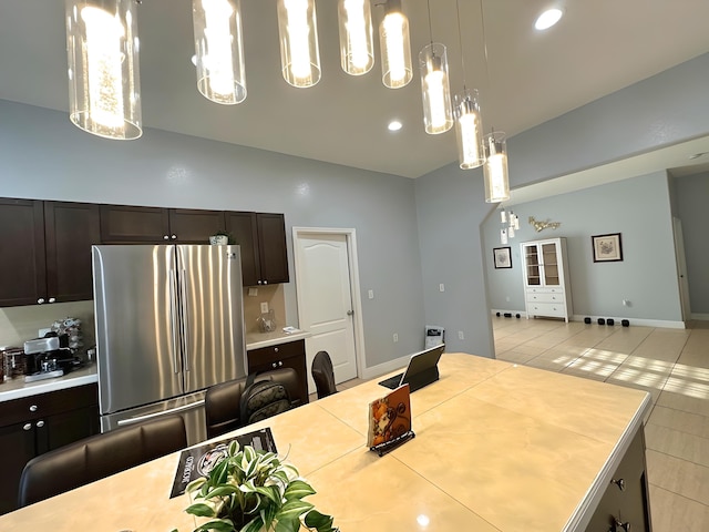 kitchen with dark brown cabinets, a center island, pendant lighting, stainless steel refrigerator, and light tile patterned floors