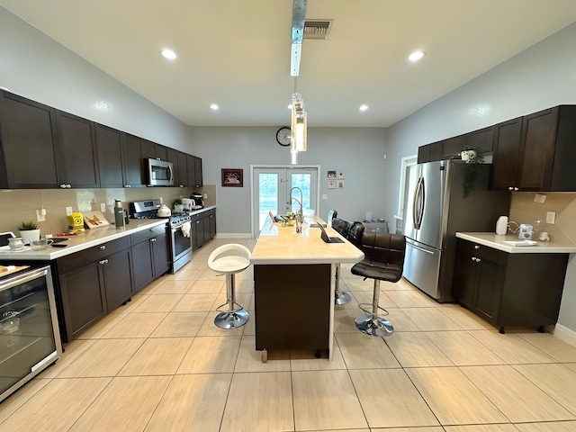 kitchen with an island with sink, a breakfast bar, pendant lighting, dark brown cabinetry, and stainless steel appliances