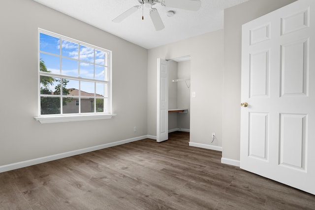 unfurnished bedroom with wood-type flooring, a spacious closet, a textured ceiling, a closet, and ceiling fan