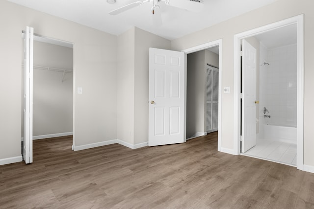 unfurnished bedroom with light wood-type flooring, a spacious closet, a closet, ceiling fan, and connected bathroom