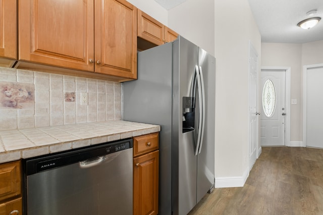 kitchen featuring decorative backsplash, tile counters, appliances with stainless steel finishes, a textured ceiling, and light hardwood / wood-style floors