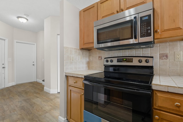 kitchen with black electric range oven, decorative backsplash, a textured ceiling, light wood-type flooring, and tile counters