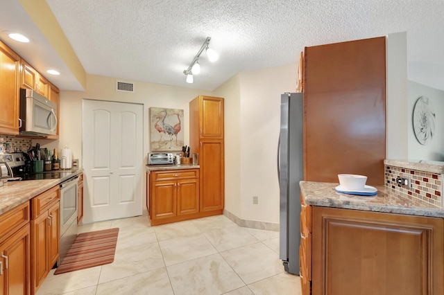 kitchen featuring appliances with stainless steel finishes, backsplash, rail lighting, light stone counters, and light tile patterned floors