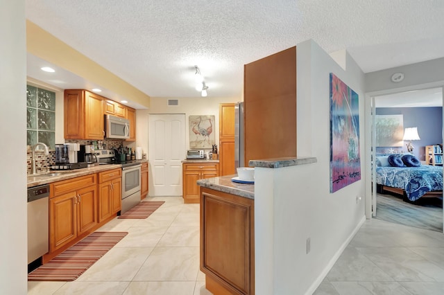 kitchen with sink, decorative backsplash, a textured ceiling, light tile patterned flooring, and stainless steel appliances