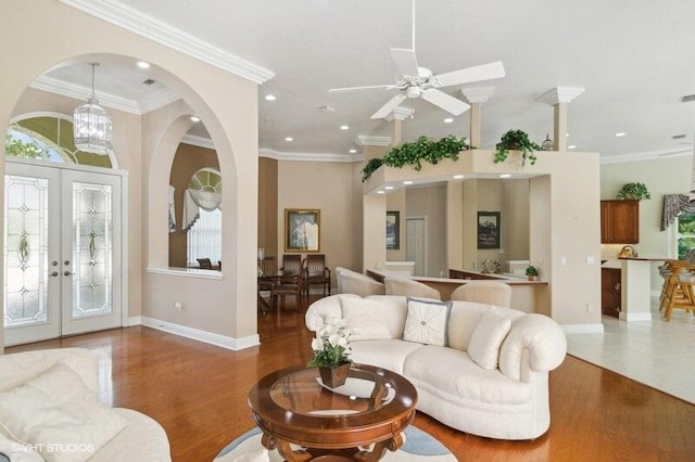 living room featuring french doors, wood-type flooring, ornamental molding, and ceiling fan with notable chandelier