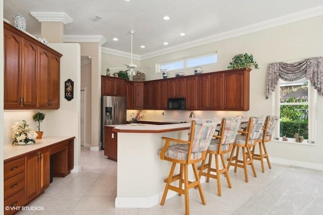 kitchen with light tile patterned floors, a center island, stainless steel fridge, crown molding, and a breakfast bar area