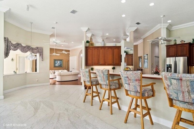 kitchen with a kitchen breakfast bar, hanging light fixtures, kitchen peninsula, ornamental molding, and stainless steel fridge