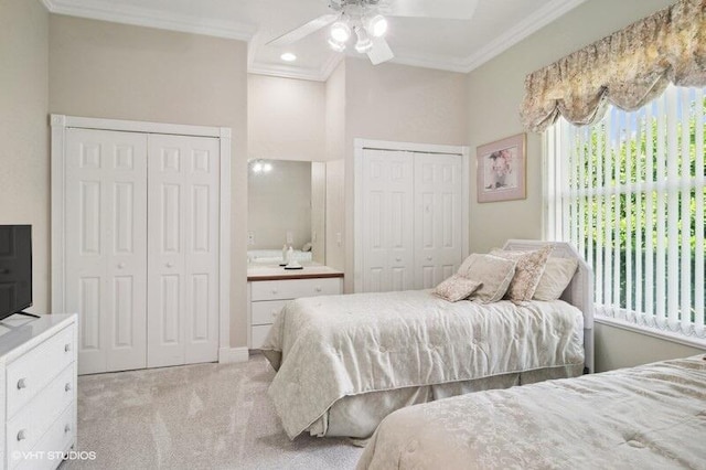 carpeted bedroom with ornamental molding, two closets, and ceiling fan