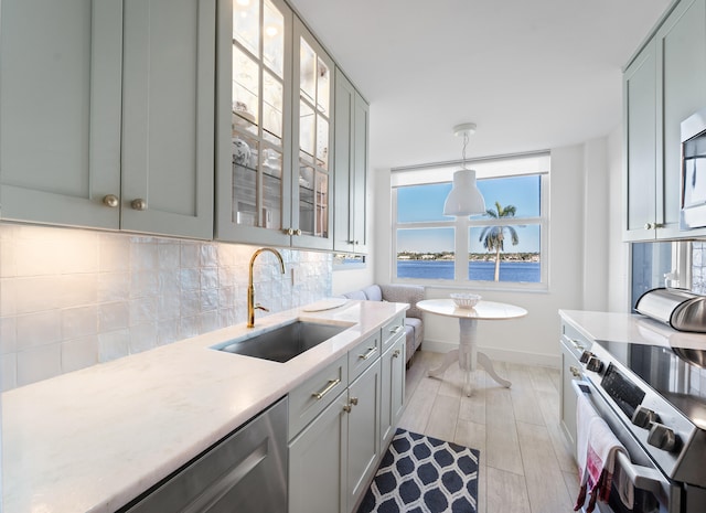 kitchen with sink, a water view, appliances with stainless steel finishes, decorative light fixtures, and light hardwood / wood-style flooring