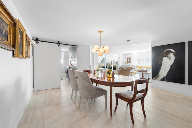 dining space with a barn door, a chandelier, and light wood-type flooring