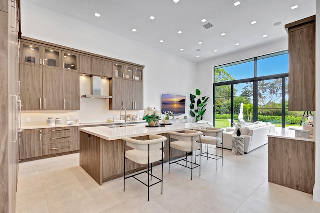 kitchen with sink, wall chimney exhaust hood, a kitchen breakfast bar, an island with sink, and light tile patterned floors