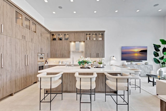 kitchen featuring a large island, sink, wall chimney exhaust hood, double oven, and a kitchen bar