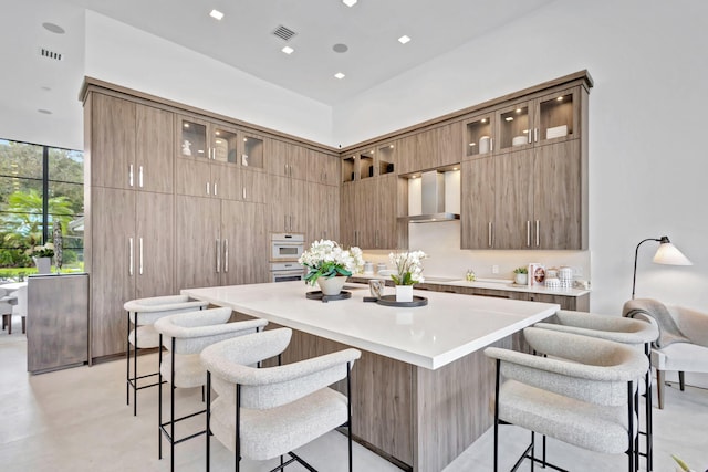 kitchen featuring a kitchen breakfast bar, white double oven, a spacious island, and wall chimney exhaust hood