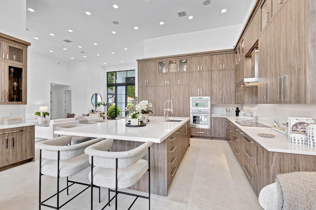 kitchen with sink, stainless steel double oven, an island with sink, a kitchen bar, and black electric cooktop