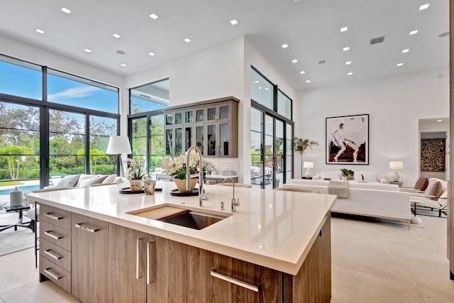 kitchen with a center island with sink, light stone countertops, sink, and light tile patterned floors