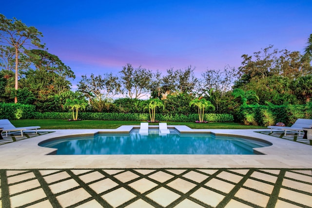 pool at dusk with a patio area and a lawn