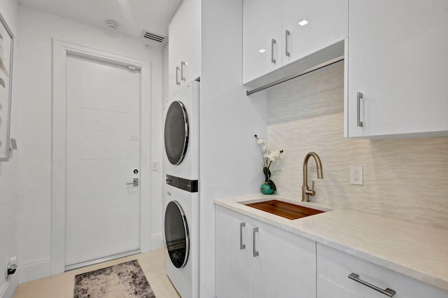 laundry area with cabinets, stacked washer and clothes dryer, and sink