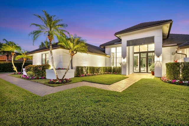 back house at dusk with french doors and a yard