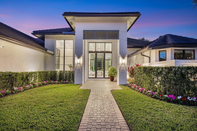 exterior entry at dusk with french doors and a lawn