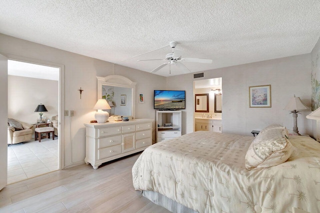 bedroom featuring a textured ceiling, connected bathroom, light wood-type flooring, and ceiling fan