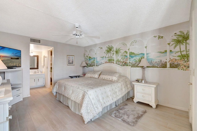 bedroom featuring ceiling fan, a textured ceiling, light wood-type flooring, and ensuite bath