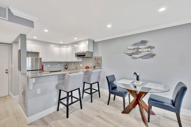 kitchen featuring light hardwood / wood-style flooring, kitchen peninsula, white cabinets, appliances with stainless steel finishes, and tasteful backsplash