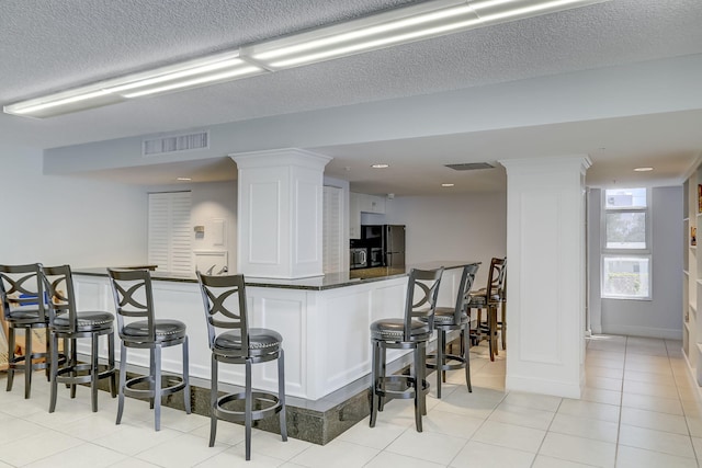 kitchen featuring ornate columns, a kitchen bar, black refrigerator, and white cabinets