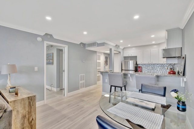 interior space with stainless steel fridge, kitchen peninsula, white cabinets, and ornamental molding