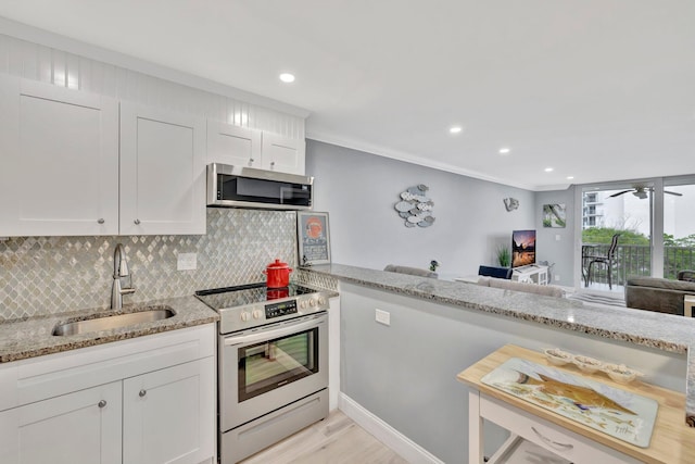 kitchen with white cabinets, light stone counters, appliances with stainless steel finishes, crown molding, and sink