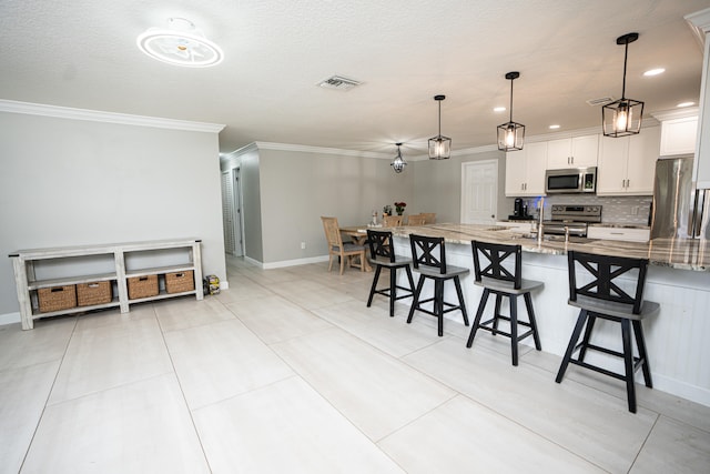 kitchen featuring a breakfast bar area, stainless steel appliances, decorative light fixtures, white cabinetry, and light stone counters