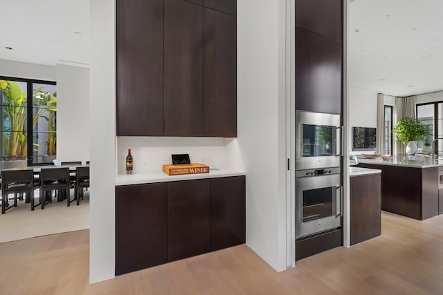 kitchen featuring oven, light hardwood / wood-style flooring, dark brown cabinetry, and a wealth of natural light