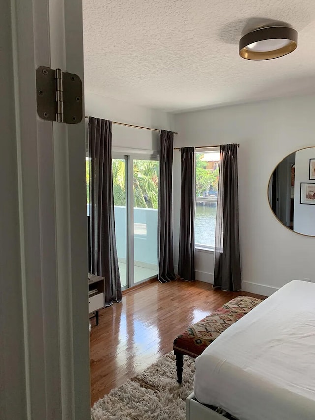 bedroom with light hardwood / wood-style flooring, a textured ceiling, and access to outside