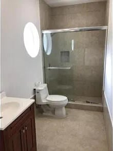 bathroom featuring a shower with door, vanity, and toilet